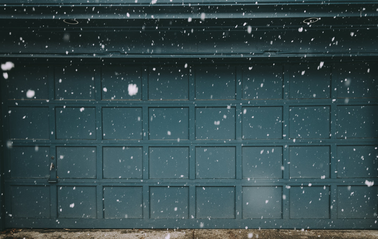 Exterior view of a modern garage door with snow falling outside