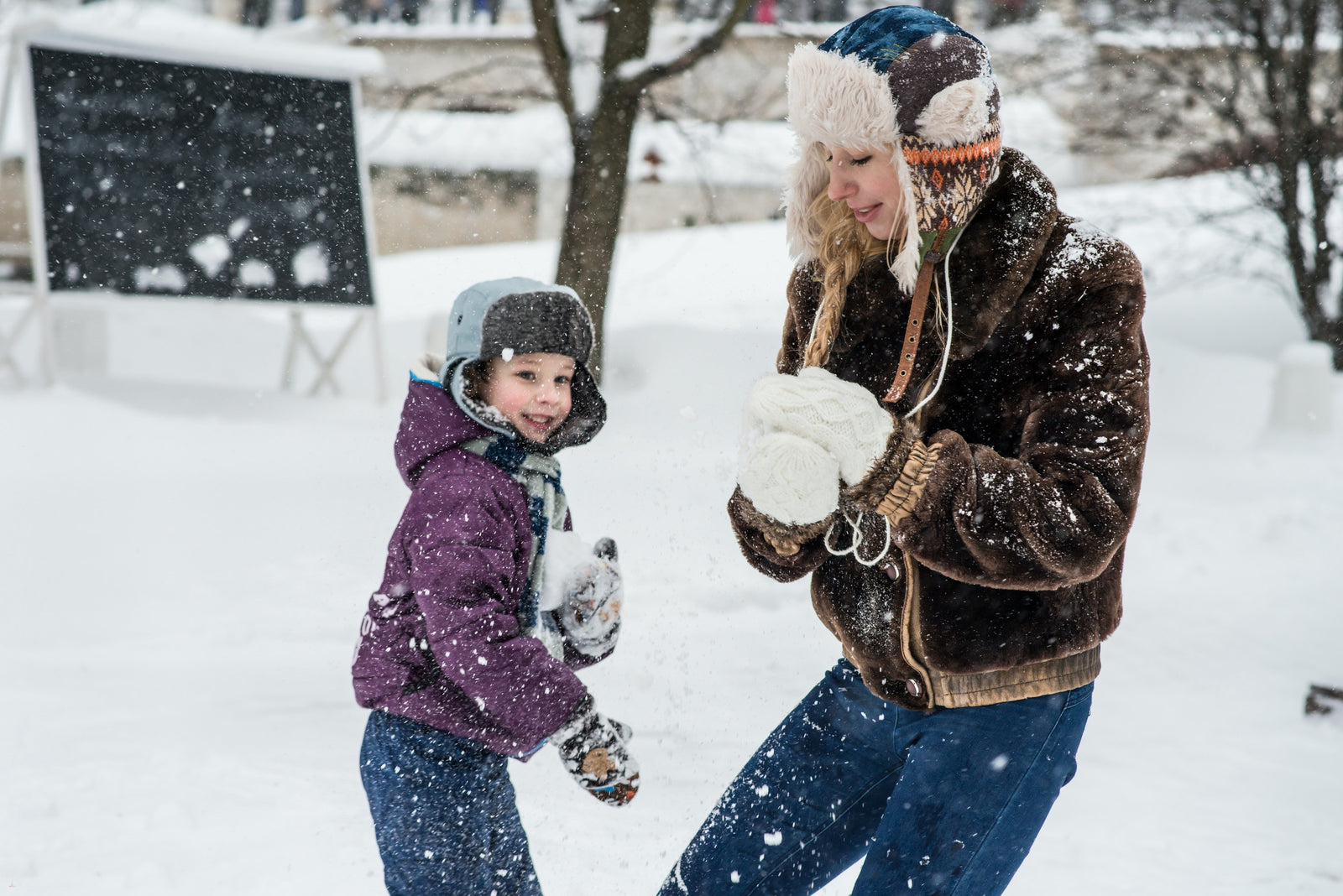 A mother and child dressed in winter clothing pack snowballs outside